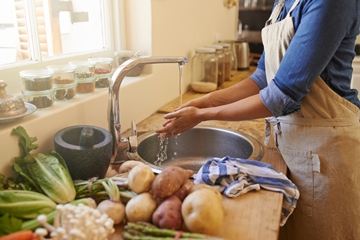 Cropped picture of an unrecognizable woman washing her hands in the kitchen sink. She's about to prepare food.