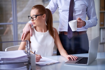 A boss standing and putting his hand on secretary's arm while she looks at his hand.