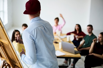 A back view of a male employee presenting to his colleagues in a boardroom