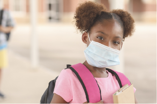 An african american school girl with her school bag on her back and carrying a book