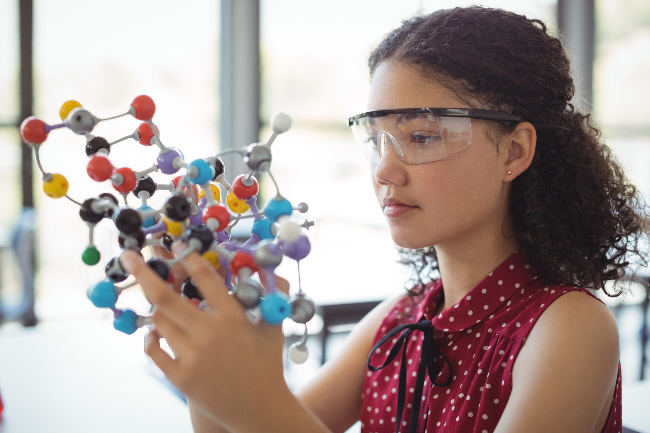 Attentive schoolgirl experimenting molecule model in laboratory at school