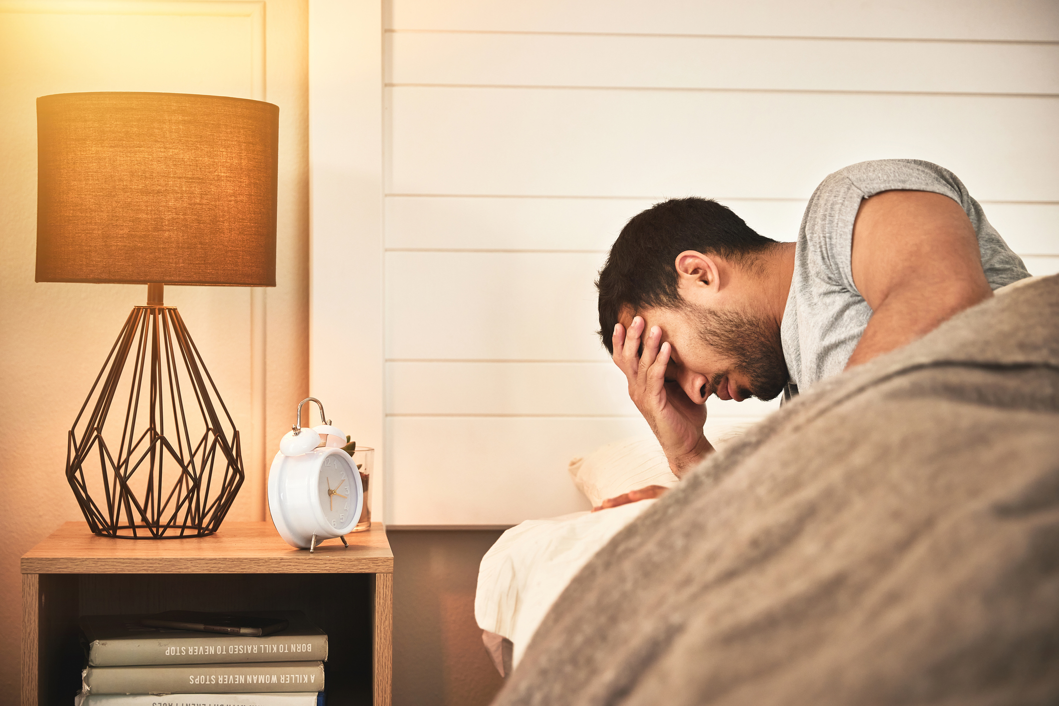 Young displeased, tired man with insomnia unable to sleep and suffering from burnout and fatigue struggling to get up out of bed in the morning. Mentally exhausted male awake in bed feeling stressed