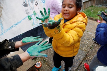 Boy with Autism playing in back yard, making hand prints on the wall, looking at his hands, holding palms up covered in green paint